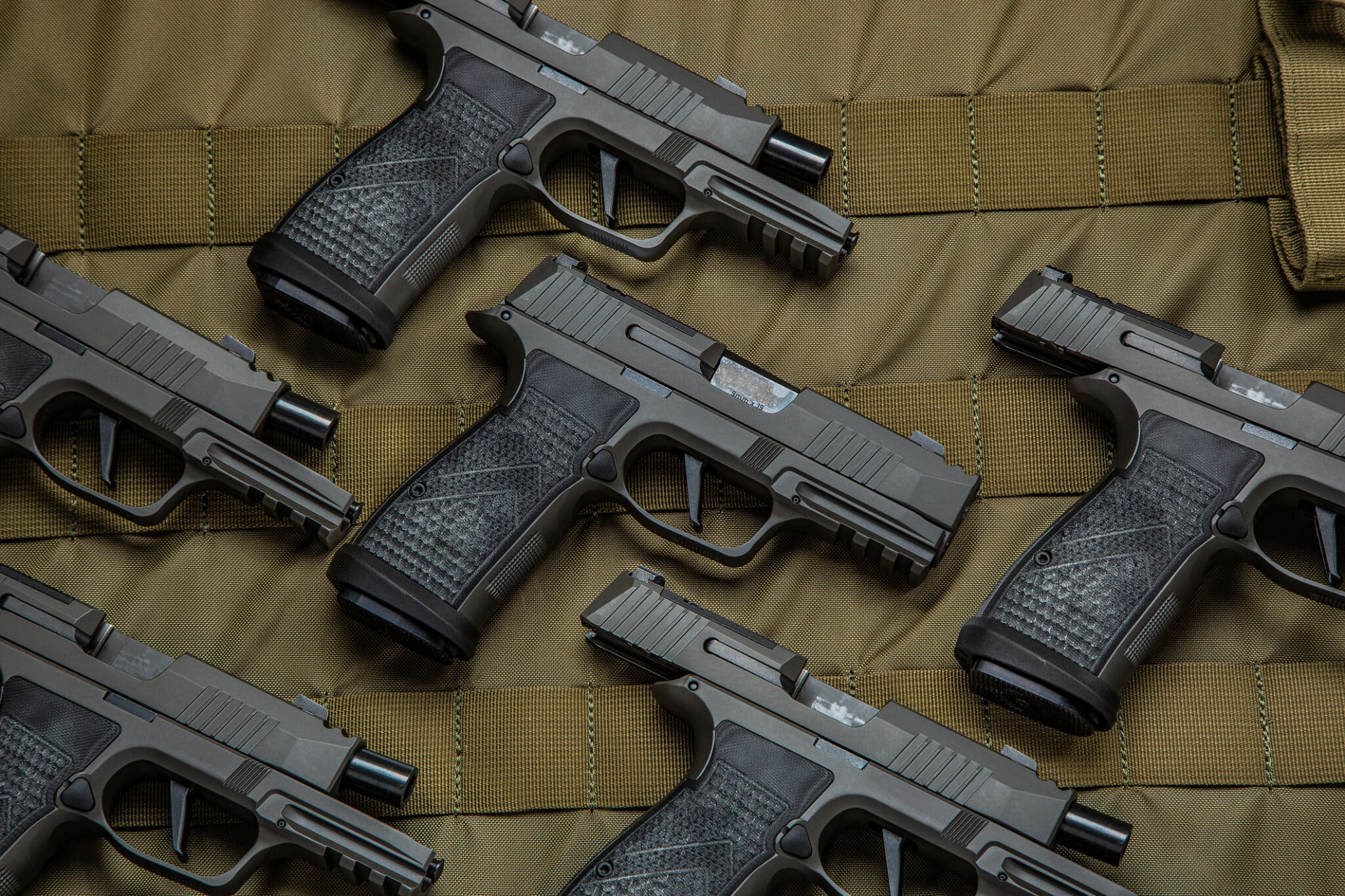 A collection of black handguns with textured grips are arranged on a khaki tactical vest, showcasing their design and features.